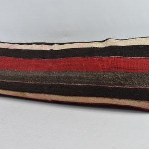 May include: A long, rectangular cushion with a striped pattern in shades of red, brown, and white. The cushion is made of a woven fabric and has a slightly textured surface.