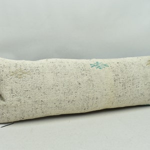 May include: A long, white, rectangular pillow with a subtle, speckled pattern. The pillow has a simple design with two small, teal-colored snowflake patterns.