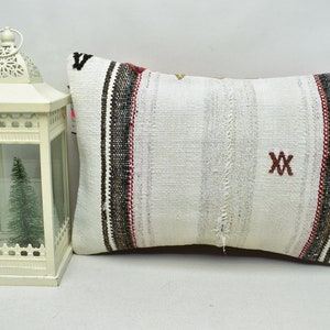 May include: White rectangular pillow with black, red, and brown stripes and embroidered red X's. The pillow is made of woven fabric and has a rustic, vintage look.