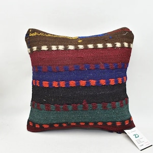 May include: A colorful striped throw pillow with a woven design in shades of red, blue, green, and black. The pillow is made of a soft, textured fabric and has a fringe trim.