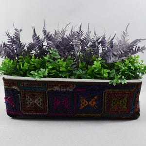 May include: A rectangular planter with a colorful embroidered design. The planter is filled with green and purple leafy plants.