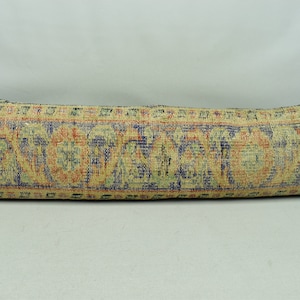May include: A long, rectangular pillow with a zipper closure. The pillow is covered in a patterned fabric with a beige background and colorful floral designs in shades of blue, red, and green.