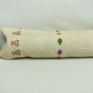 May include: A long, off-white cushion with embroidered geometric patterns in shades of green, brown, pink, and orange.