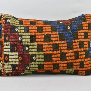 May include: A rectangular cushion with a brown, orange, red, blue and white geometric pattern. The cushion is made of woven fabric and has a fringed edge.