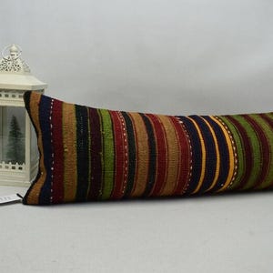 May include: A long, rectangular cushion with a striped pattern in shades of red, green, blue, and gold. The cushion is a decorative item, likely for a bed or sofa. The cushion's dimensions are not visible.