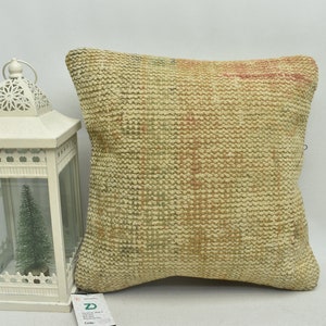 May include: A square, beige throw pillow with a woven texture. The pillow has a subtle pattern of pink, green, and brown throughout.