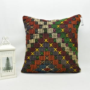 May include: A square pillow with a colorful geometric pattern. The pattern is made up of squares and crosses in shades of red, orange, yellow, green, blue, and brown.