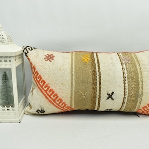 May include: A white rectangular pillow with a brown, orange, and white geometric pattern. The pillow has a fringe border and is made of woven fabric.