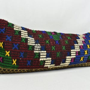 May include: A long, rectangular cushion with a colourful geometric pattern. The cushion is made of woven fabric and has a fringe border. The colours in the pattern include red, blue, green, yellow, and white.