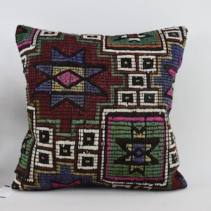 May include: Square cushion with a geometric pattern in shades of burgundy, green, blue, and pink. The cushion features a textured, woven design with a mix of shapes and colours, creating a vibrant and eye-catching look.