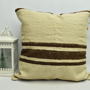May include: A cream-colored pillow with brown stripes. The pillow is made of a soft, woven fabric and has a slightly textured surface.