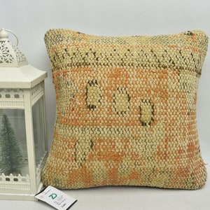 May include: A beige and orange woven throw pillow with a geometric pattern. The pillow is made of a soft, textured fabric and has a subtle sheen.