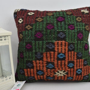 May include: A colourful throw pillow with a geometric pattern in shades of red, green, orange, blue, and brown. The pillow is made of woven fabric and has a fringed edge.
