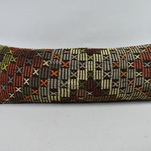 May include: A long, rectangular pillow with a brown, red, green, and cream geometric pattern. The pillow is made of woven fabric and has a traditional design.