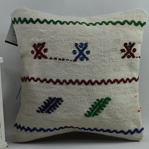 May include: White throw pillow with colourful embroidered designs. The pillow features a geometric pattern, a leaf design, and a zig-zag border.