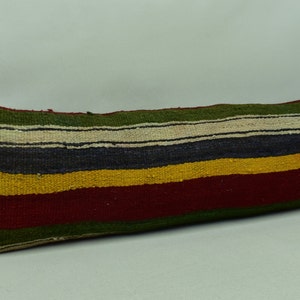 May include: A long, rectangular cushion with a striped pattern in shades of green, white, blue, yellow, and red. The cushion is made of woven fabric and has a rustic, handmade look.