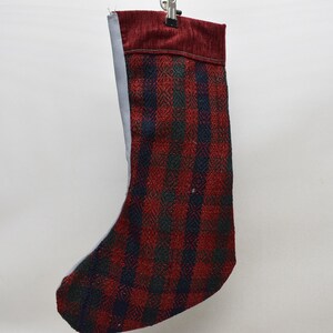 Op de afbeelding: Een kerstsok met een rood, zwart en groen ruitpatroon. De bovenkant van de sok is effen bordeauxrood. De binnenkant van de sok is lichtgrijs.
