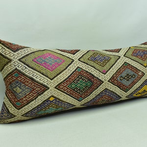 May include: A long, rectangular pillow with a geometric pattern in shades of brown, beige, red, blue, green, and yellow. The pattern features a series of squares with intricate designs.