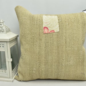 May include: A beige throw pillow with a floral fabric patch sewn on the front. The pillow is made of a textured fabric and has a blue trim around the edges.