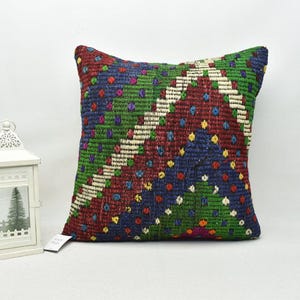 May include: A colourful square cushion with a geometric pattern in shades of red, green, blue, and white. The cushion is made of woven fabric and has a fringed edge.