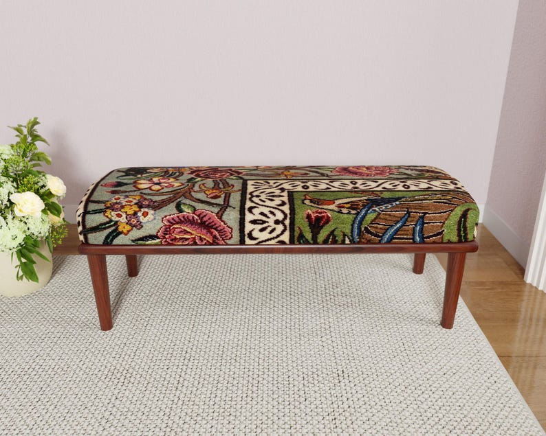 Puede incluir: Banco rectangular con un coj&iacute;n estampado floral en tonos verdes, rosas y marrones. El banco tiene un marco de madera marr&oacute;n oscuro y cuatro patas anguladas. El coj&iacute;n presenta un dise&ntilde;o bot&aacute;nico detallado.