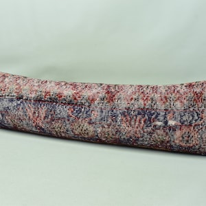 May include: A long, rectangular cushion with a colourful, patterned fabric. The fabric features a mix of red, blue and white colours in a floral design.