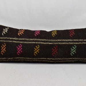 May include: A long, rectangular black pillow with a woven pattern of colorful geometric shapes. The pillow has a striped design with two white stripes.