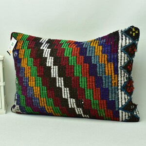 May include: A colourful rectangular cushion with a geometric pattern in shades of red, green, blue, yellow, and white. The cushion is made of woven fabric and has a fringed edge.