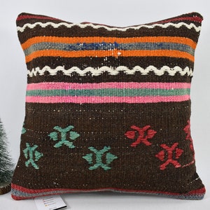 May include: A brown, square cushion with a colourful striped pattern and geometric designs. The cushion is made of woven fabric and has a fringed edge.