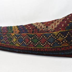 May include: A long, rectangular cushion with a colourful, geometric pattern. The cushion is made of woven fabric and has a fringe border. The cushion is lying on a white surface.