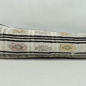 May include: A long, rectangular cushion with a white background and black stripes. The cushion is decorated with a geometric pattern in shades of brown, gold, and pink.