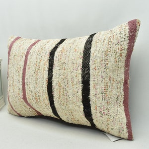 May include: A rectangular throw pillow with a white background and pink, black, and orange stripes. The pillow is made of a woven fabric and has a slightly textured surface.