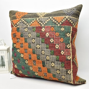 May include: A square throw pillow with a colorful geometric pattern in shades of orange, green, red, and gray. The pillow is made of woven fabric and has a fringed edge.