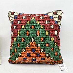 May include: A colourful throw pillow with a geometric pattern in shades of red, green, orange, and blue. The pillow is made of woven fabric and has a fringe border.