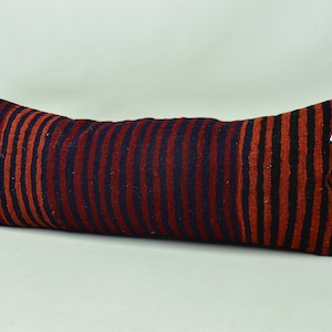 May include: A long, rectangular cushion with a striped pattern in shades of red, black, and blue. The cushion is made of a woven fabric and has a slightly textured surface.