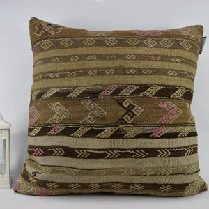 May include: A brown and beige patterned cushion with pink accents. The cushion is made of woven fabric and has a geometric design.