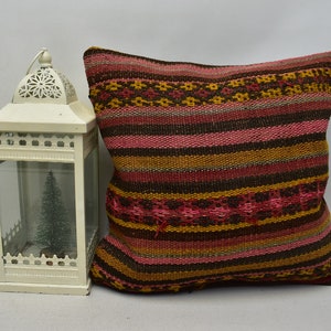 May include: A decorative pillow with a striped pattern in shades of brown, pink, and gold. The pillow is made of woven fabric and has a slightly textured surface.