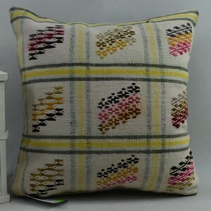 May include: A white cushion with a yellow, grey, and white plaid pattern. The cushion has a colourful embroidered design of stylised leaves in shades of pink, red, yellow, and brown.