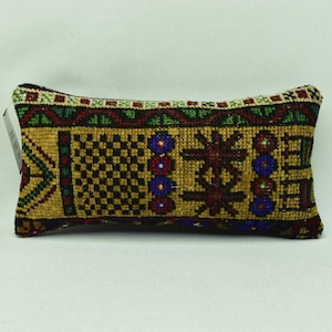 May include: Embroidered rectangular cushion with a detailed pattern. The design features gold, brown, and burgundy central motifs, with blue, green, and red accents. The edges are trimmed with a patterned border. Measurements are not available.