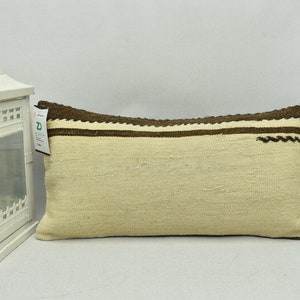 May include: A white and brown woven cushion with a decorative border. The cushion is rectangular and has a soft, textured surface.