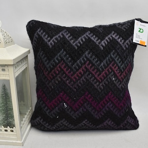 May include: Black and purple patterned throw pillow with a zig-zag design. The pillow has a tag with the letter "D" on it.