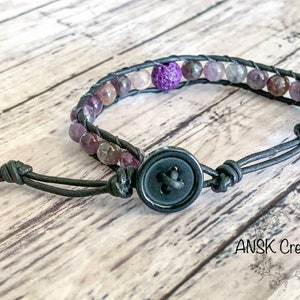 May include: A black leather bracelet with a button closure and purple and brown gemstone beads.