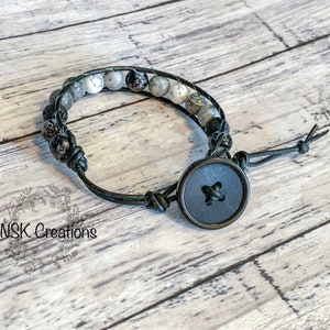 May include: A black leather bracelet with a black button closure. The bracelet features black and white beads.