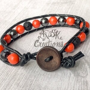 May include: A black leather bracelet with orange and black beads, a wooden button closure, and the text "A&S Creations".