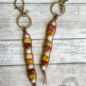 May include: Two leather keychains with brown leather cord and wooden beads in shades of red, yellow, and white. The keychains have silver key rings.