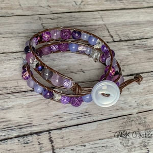 May include: A triple wrap leather bracelet with purple and blue gemstone beads and a white button closure.