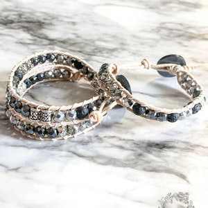 May include: Three layered bracelets with black and silver beads, black lava beads, and silver accents. The bracelets are on a white marble surface.