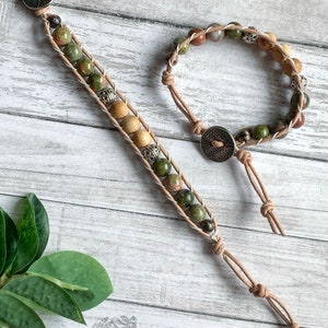 May include: Two leather bracelets with green and brown stone beads and silver accents. The bracelets are tied with leather cords and have a button closure.