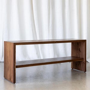 May include: A dark brown wooden bench with a single shelf. The bench has a simple, modern design and is made of solid wood.