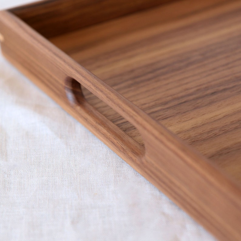 Puede incluir: Una bandeja de servir de madera con un acabado de madera natural y una forma rectangular. La bandeja tiene un asa integrada en un lado.